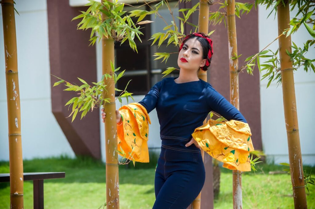 Elegant woman in traditional attire posing among bamboo plants outdoors.