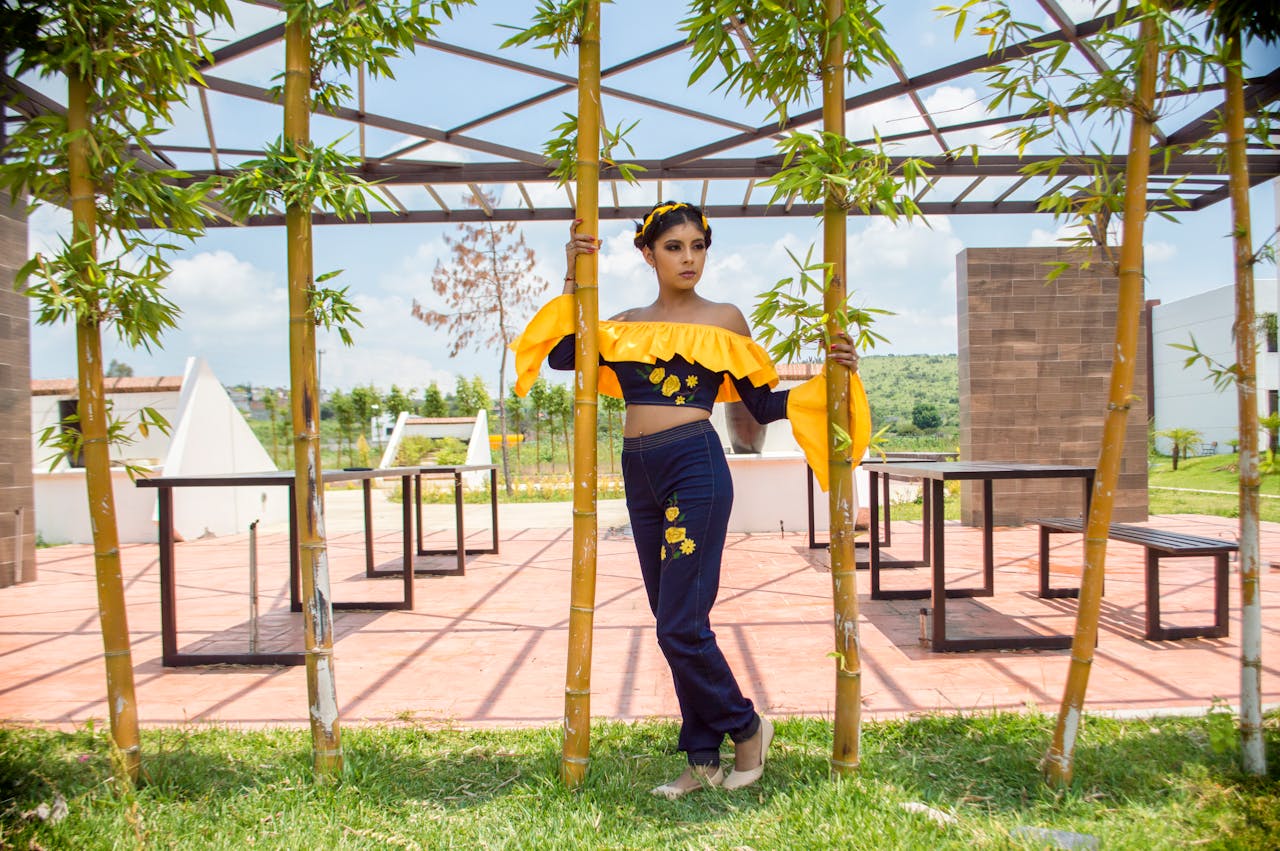 Stylish woman in vibrant yellow and blue outfit poses in a bamboo garden on a sunny day.