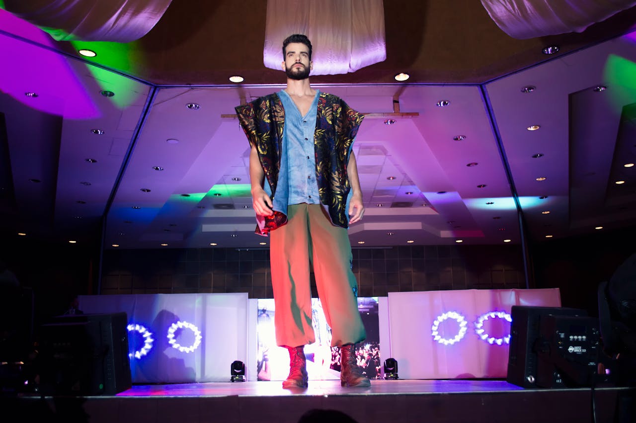 A confident male model walks the runway at a vibrant fashion show indoors.