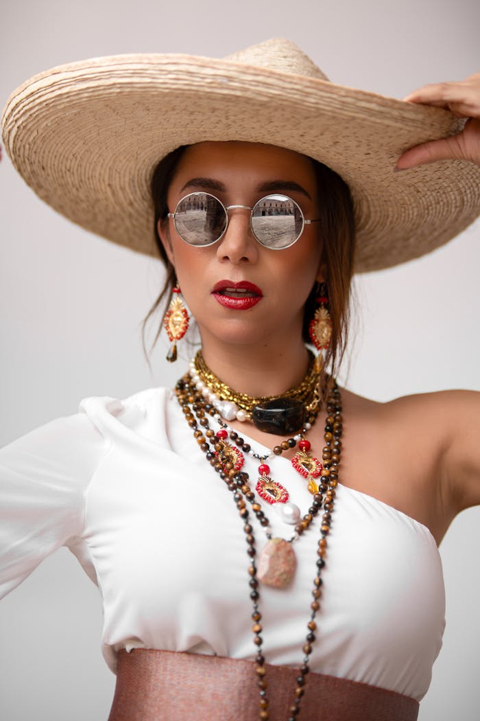 Stylish woman in white top and hat wearing vibrant jewelry in a studio shot.